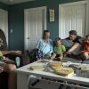 Megan and Stephen Alger, as well as four of their children, are situated around a coffee table in their home. Megan Alger and two of her sons are seated on a sofa. An older son and a toddler-age son are seated in an armchair, and Stephen Alger is behind the sofa. The three younger boys have books in their laps, and children's books are scattered on the coffee table.