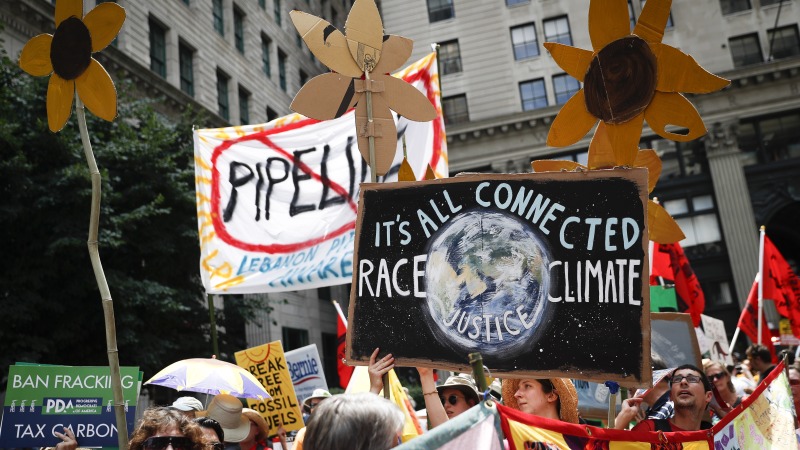 Climate change activists carry signs as they march during a protest in Philadelphia in 2016. Earlier that year, U.S. prosecutors allege hackers began targeting prominent American climate activists in an effort to gather information to foil lawsuits against the fossil fuel industry over damage communities have faced from global warming.