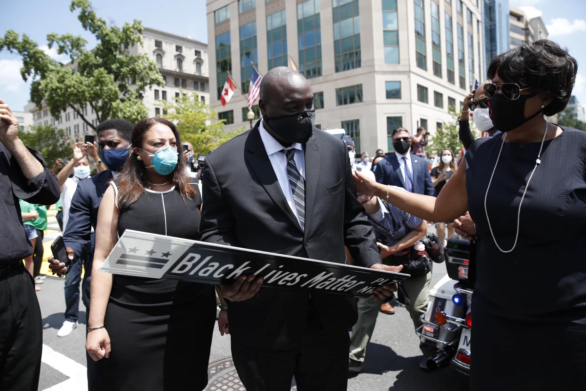 District of Columbia Mayor Muriel Bowser (R) presents a Black Lives Matter Plaza street sign to a representative of the family as the hearse with the flag-draped casket of U.S. congressman and civil rights icon John Lewis drives on 16th Street, renamed Black Lives Matter Plaza, near the White House in Washington, DC July 27, 2020.