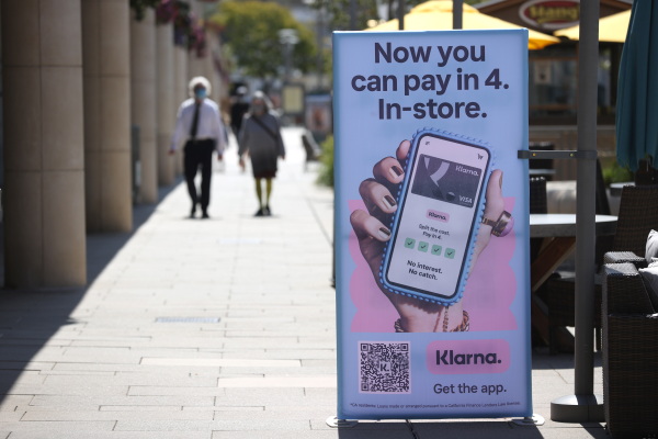 Pedestrians walk toward a sidewalk sign that reads "Now you can pay in 4. In-store" with a picture of a hand holding a cellphone.