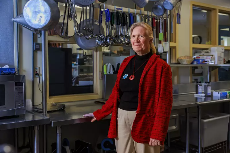 Mary Emerson is standing in the school's kitchen. Behind her is a shiny metal food preparation surface, and large spoons and ladles hang from a metal rod above.
