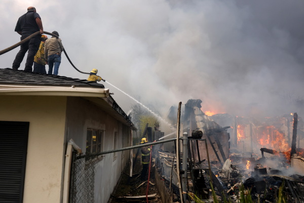 People assist firefighters with a hose line as they extinguish a burning home during the Eaton fire on Wednesday.