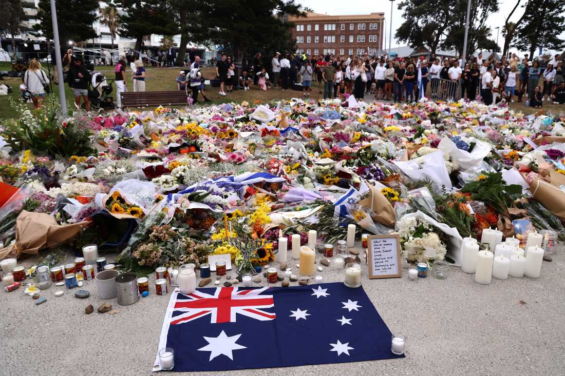 TOPSHOT - Mourners gather around floral tributes at Bondi Pavilion to honor the victims of the Bondi Beach shooting in Sydney on December 16, 2025. A father-and-son team toting long-barrelled guns shot and killed 15 people including a 10-year-old girl at Sydney's Bondi Beach on December 14, with authorities labelling it an antisemitic terrorist attack on a Jewish festival.