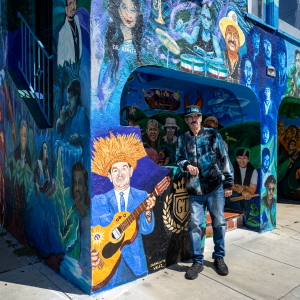 Richard Segovia stands in front of his house on 25th and York streets, known as the Latin Rock House, in San Francisco on April 7, 2026. The home is covered in a large mural honoring dozens of musicians tied to the Mission District’s Latin rock scene, which Segovia has helped preserve for decades.