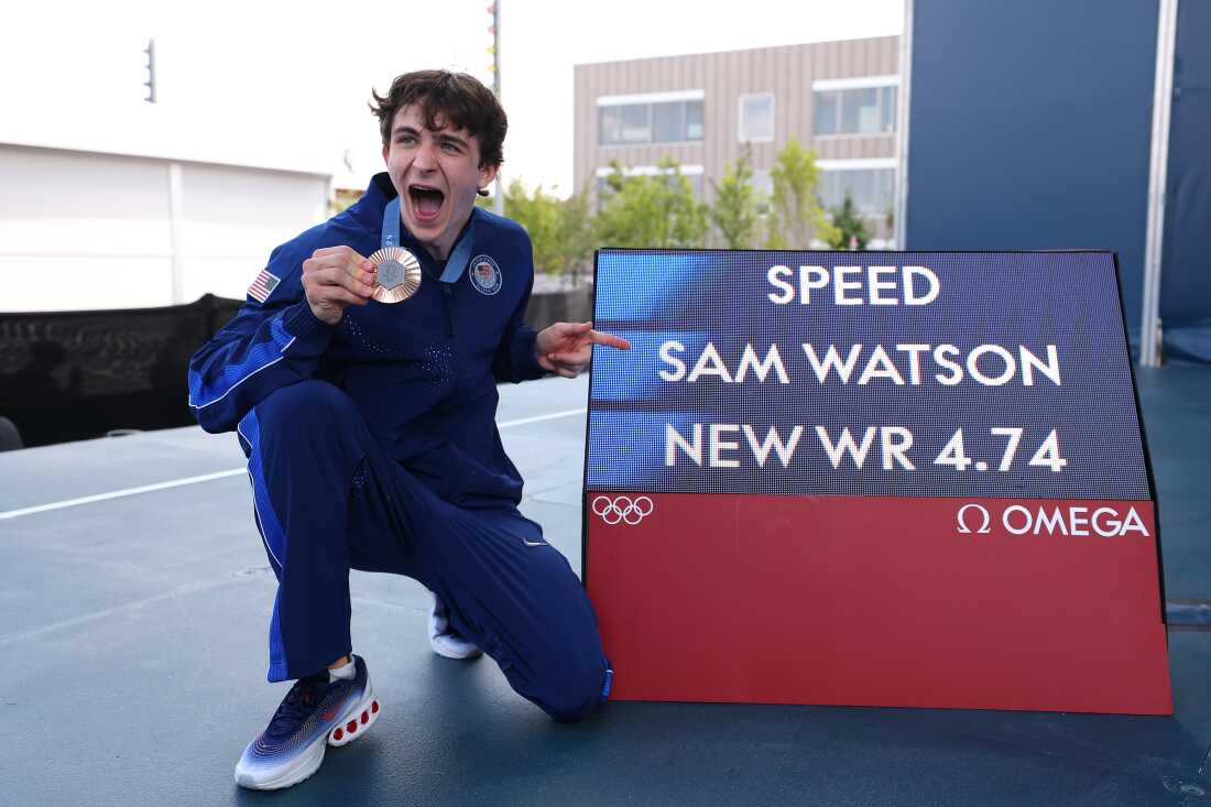 Sam Watson of Team USA poses with his bronze medal alongside a screen with his world record time of