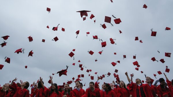 Students in red graduation gowns toss their mortarboards in the air at a commencement ceremony.