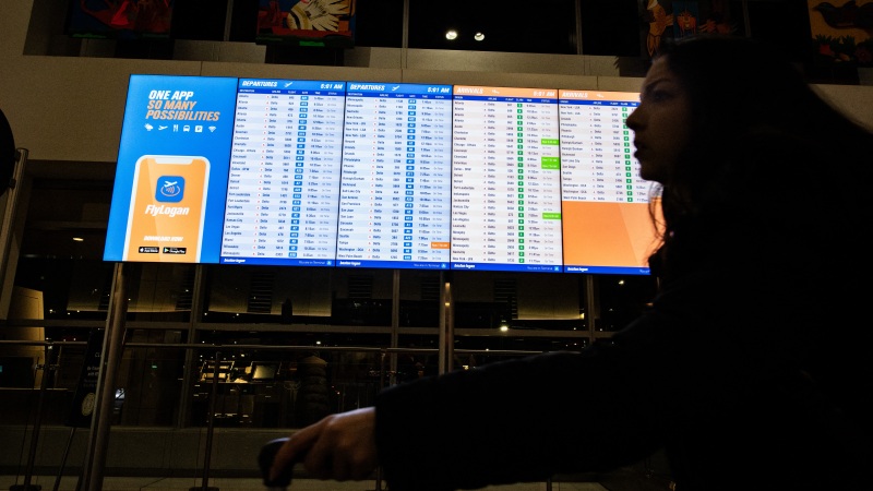 A person walks by an arrival and departure board at Boston's Logan Airport on Dec. 23, 2024.