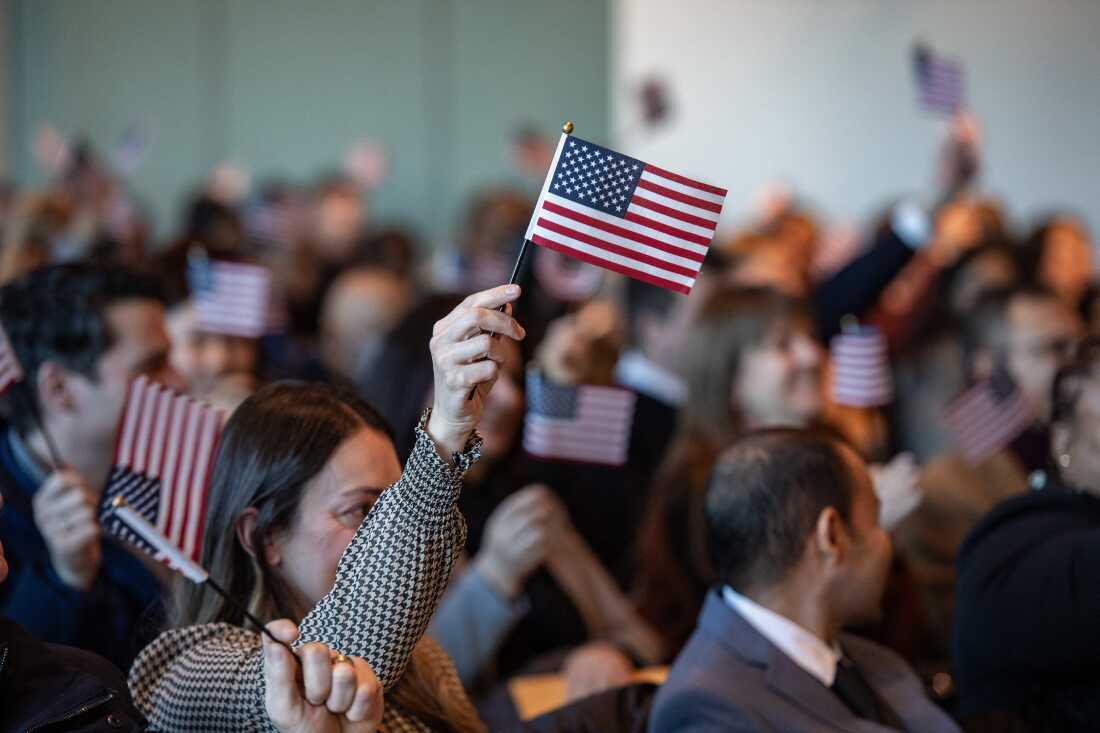 People wave U.S. flags to celebrate becoming U.S. citizens after taking the oath of allegiance during a naturalization ceremony in Boston in January 2025.