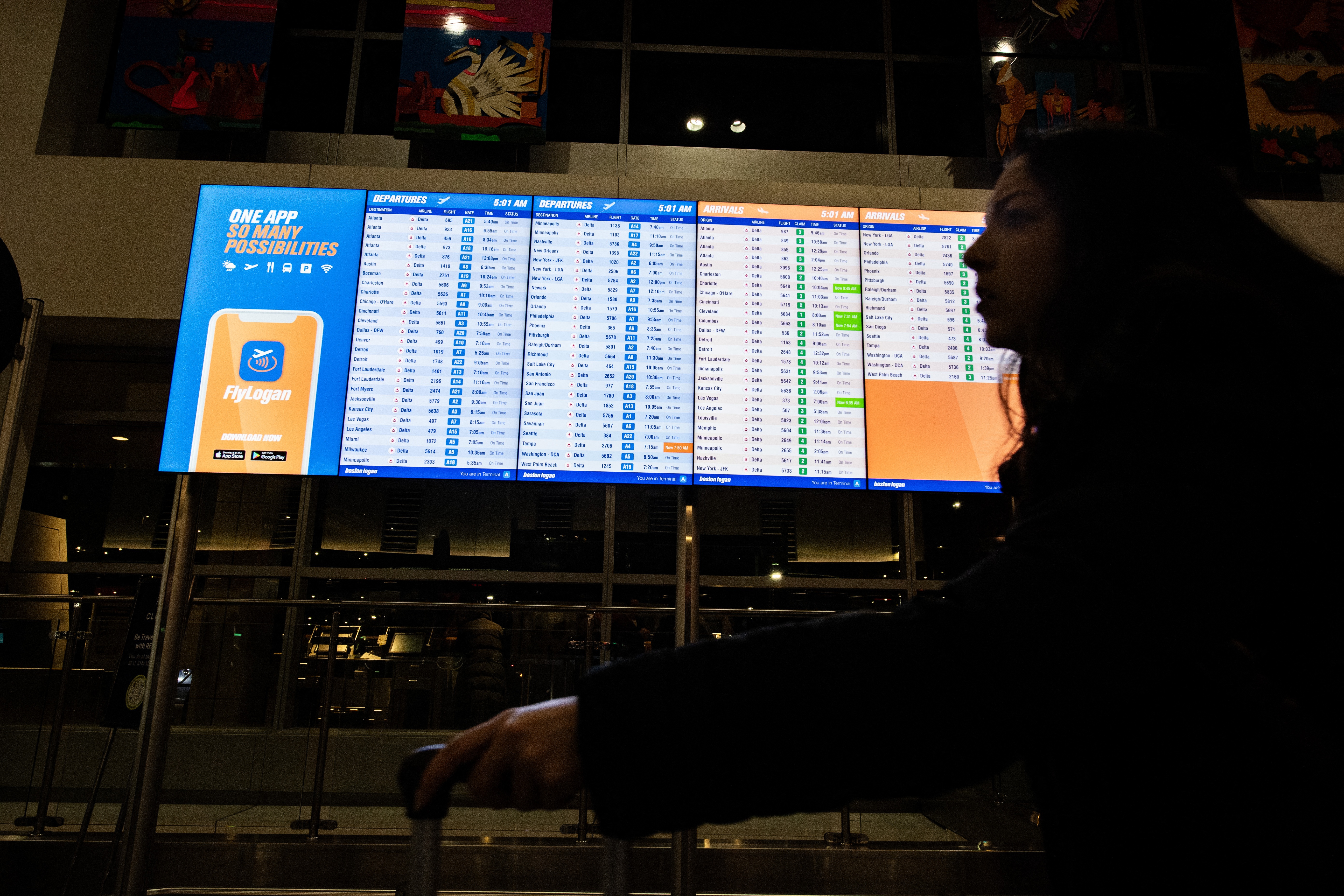 A person walks by an arrival and departure board at Boston's Logan Airport on Dec. 23, 2024. (AFP via Getty Images)