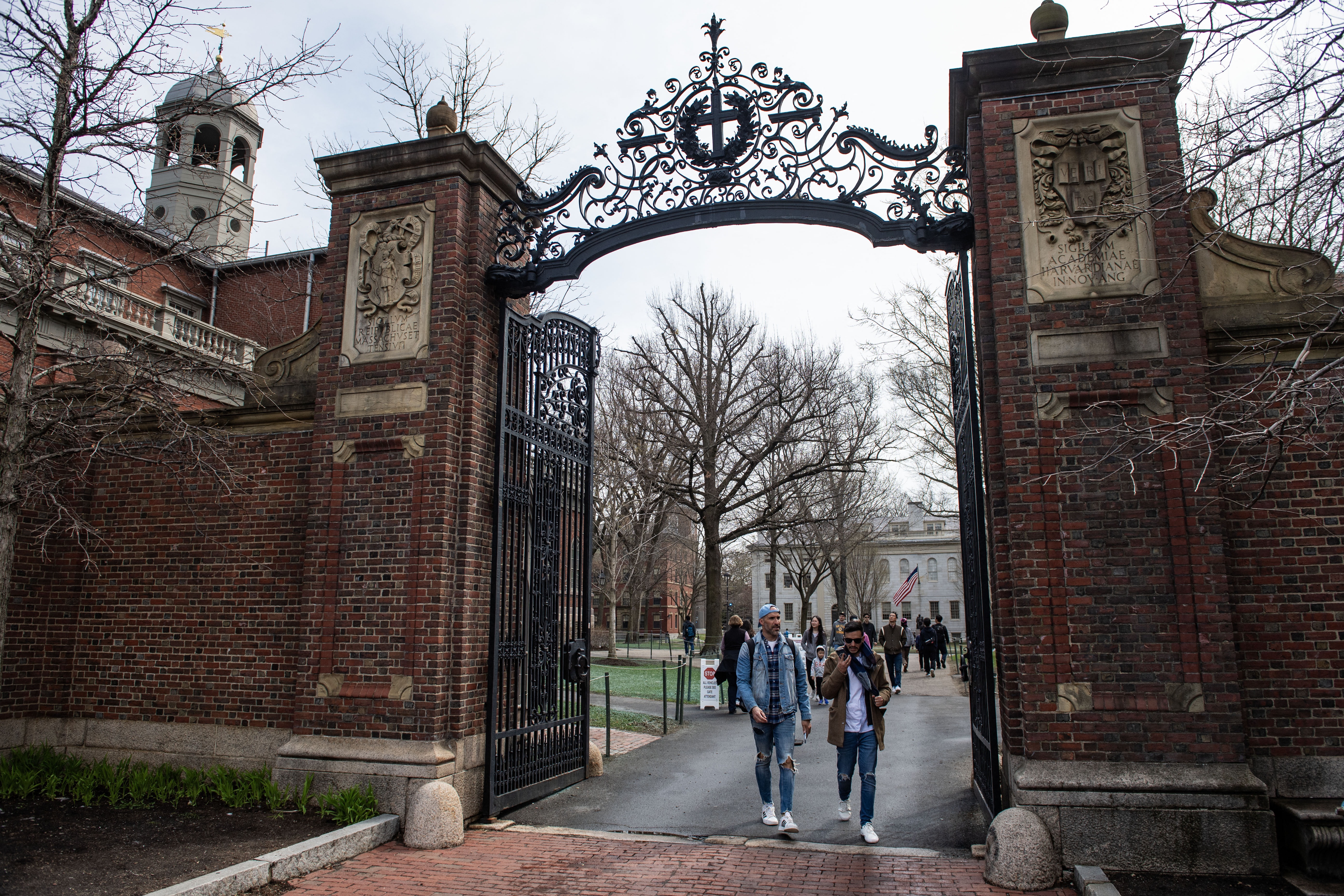 People walk through a gate as they exit Harvard Yard on the campus of Harvard University in Cambridge, Mass.