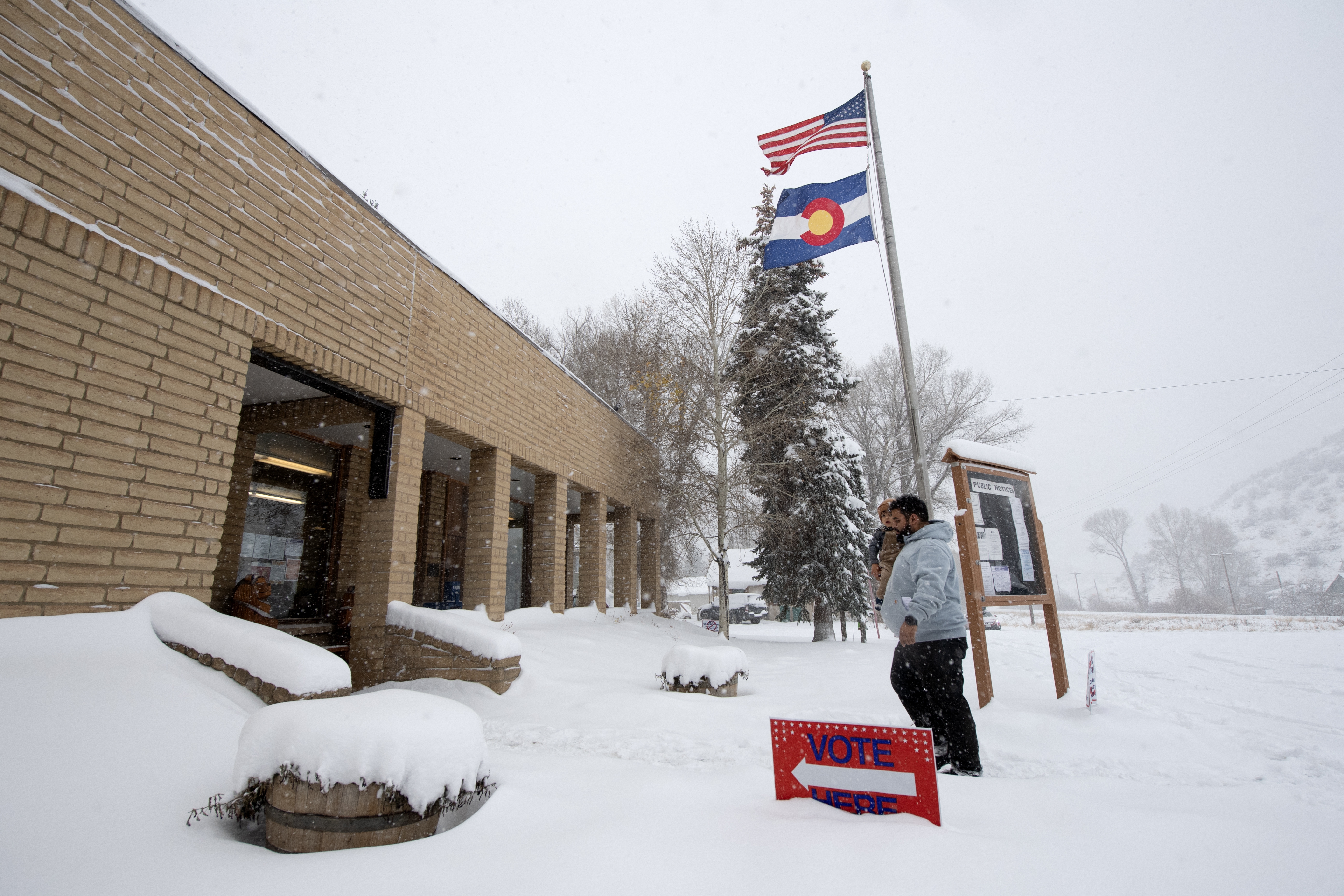 A voter carries his son as he walks into the Oak Creek Town Hall to drop off his ballot on Election Day, Nov. 5, 2024, in Oak Creek, Colo.