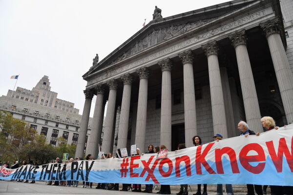 This photo shows climate activists protesting outside New York state's Supreme Court building in 2019 in New York City. They are holding a long banner that says "MAKE THEM PAY" and "#ExxonKnew."