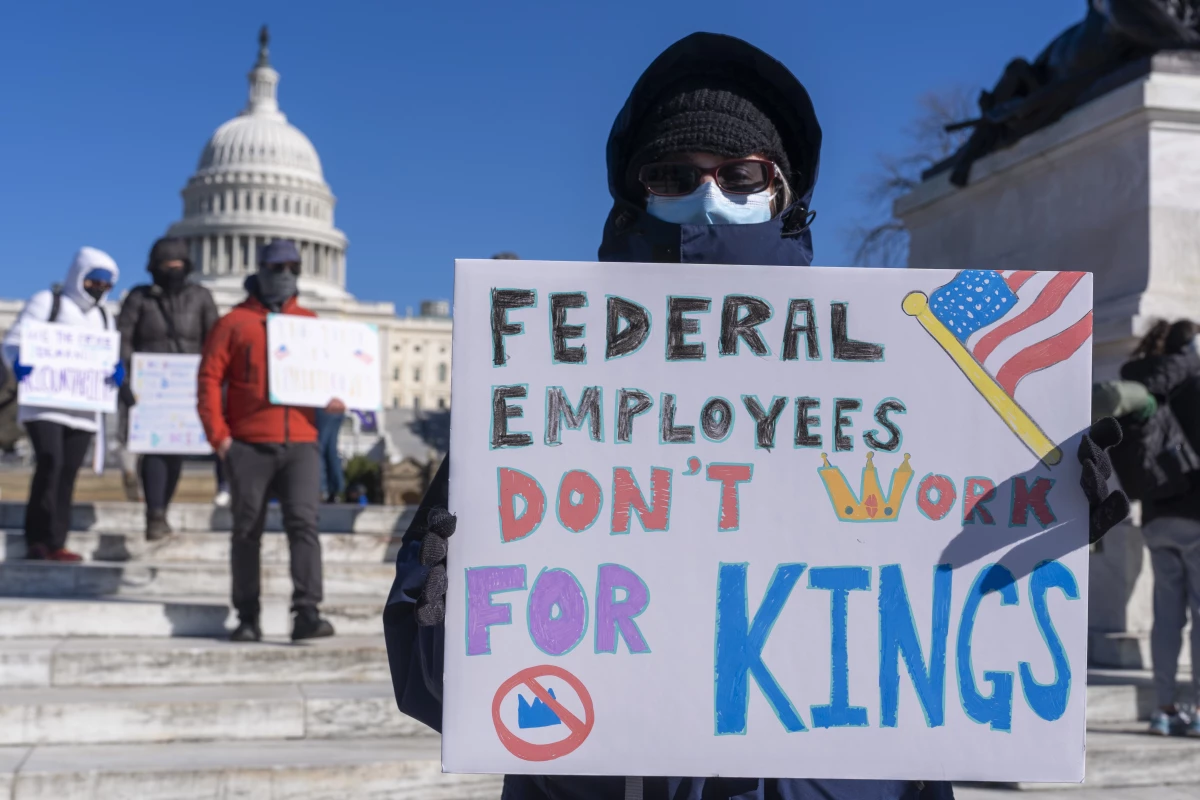 A protester with a sign saying 'Federal Employees Don't Work for Kings' demonstrates in support of federal workers and against recent actions by President Trump and Elon Musk on Presidents Day in Washington, D.C.