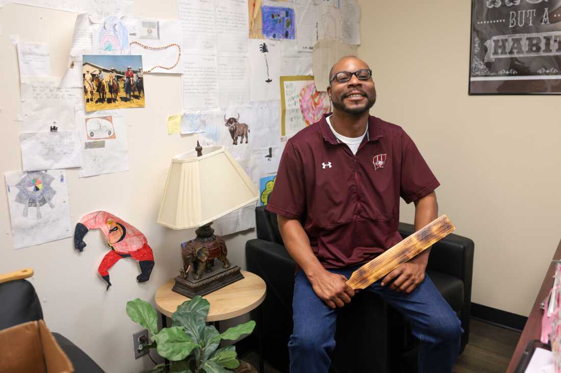 Warner Elementary School principal Alan Gordon holding one of the school paddles. Students’ drawings decorate the wall of his office.