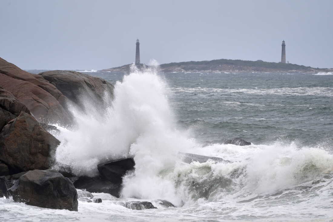 Surf breaks along the rocky coastline, with the twin lighthouses of Thatcher Island visible in the distance, during the early stages of a nor’easter Friday, Sept. 25, 2026, in Gloucester, Mass.