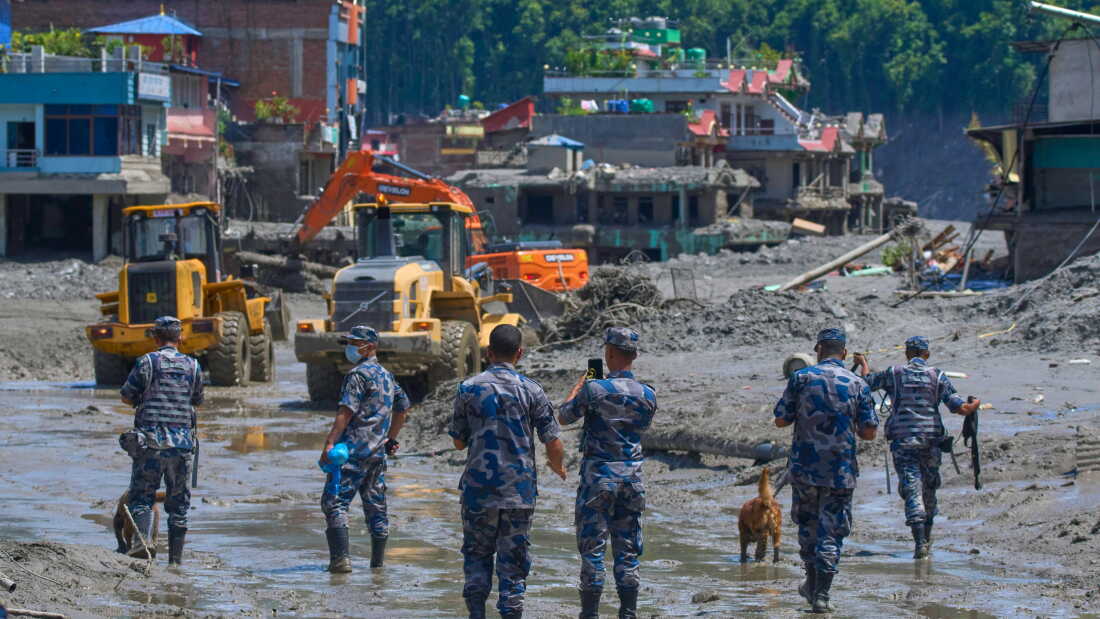 Nepalese police officers stand in thick mud as earthmovers clear the debris of flash flooding.