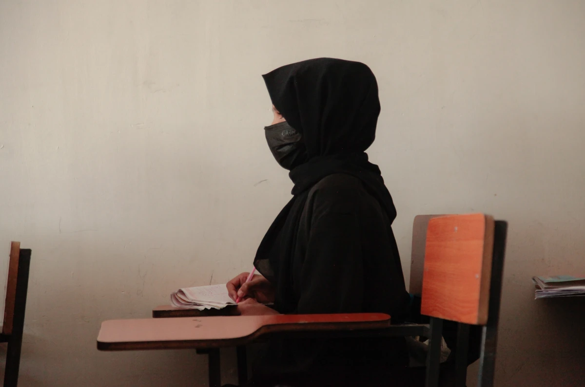 A teenage girl wearing a face mask, head scarf and long black robe, listens to a math teacher at a tutoring center in Kabul. The center was established by a women's rights activist to circumvent a Taliban ban on girls attending secondary school. The activist said she has informal permission by Taliban authorities to run the center as long as teenage girls abide by a strict dress code.
