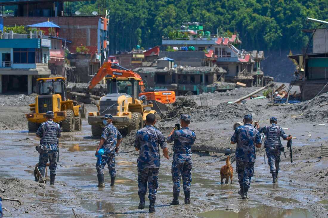 Nepalese policemen watch as earthmovers clear the debris of flash flooding in Nepal's Nuwakot district, Thursday, Aug. 27, 2026. (AP Photo/Niranjan Shrestha)