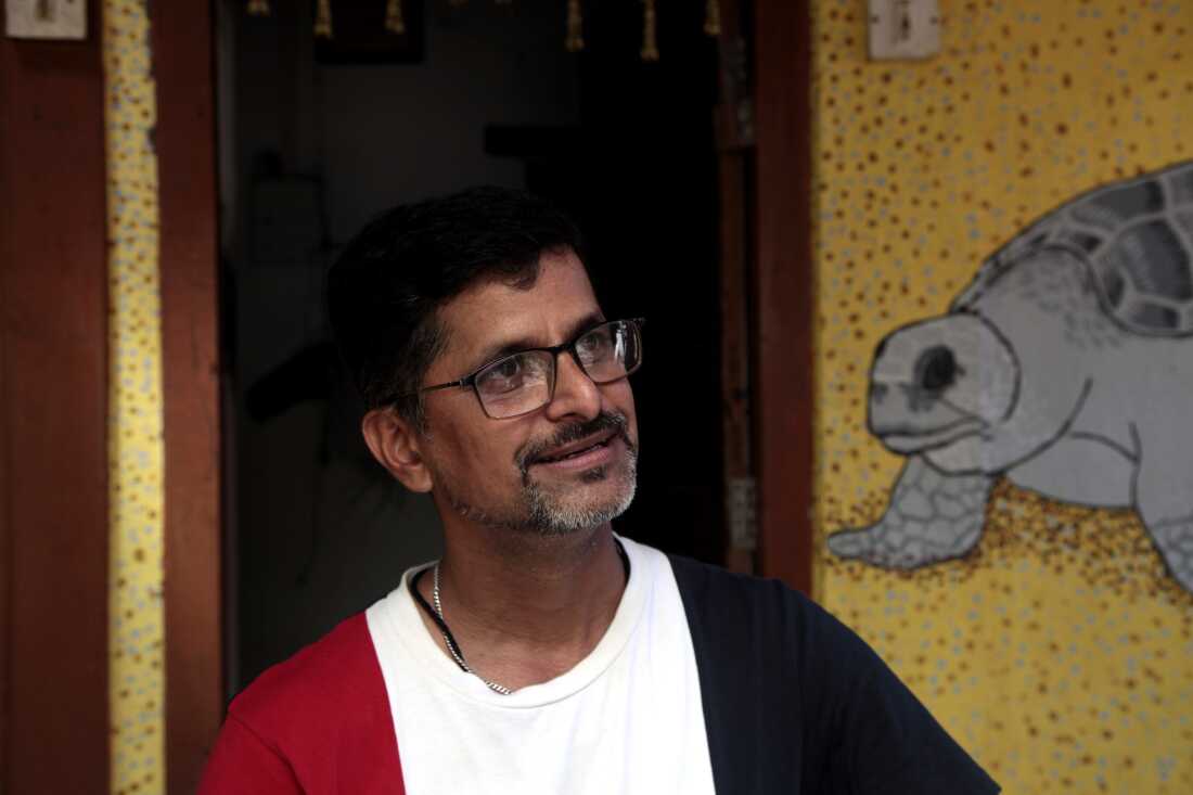 Mohan Upadhye poses for an image in his home in the western Indian village of Velas painted with the main attraction: Olive Ridley sea turtles. Upadhye is the brainchild of an eco-tourism project here, the Velas Turtle Festival. They invite people to stay in residents homes, and watch hatchings enter into the sea. This is one of the many patchwork efforts to boost the numbers of threatened Olive Ridley turtles after conservationists feared their populations would collapse in earlier decades amid industrial-scale slaughter for meat and leather, egg poaching, coastal developments on their nesting sites and their entanglement in fishing nets. Image by Diaa Hadid. April 2025, Velas, India.