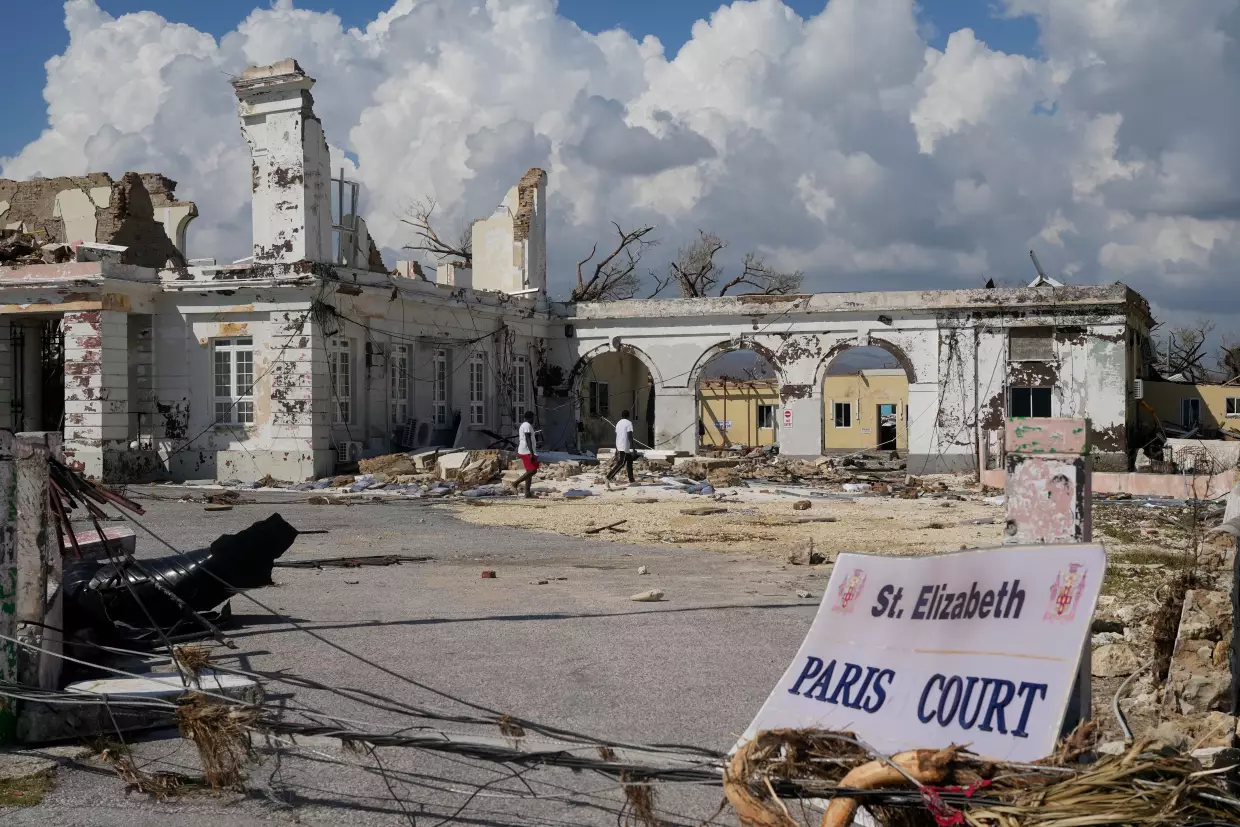 People walk past damage from Hurricane Melissa in Black River, Jamaica on Thursday, Oct. 30, 2025. Federal forecasters predict 8 to 14 named storms, including tropical storms and hurricanes, will form in the Atlantic in 2026.