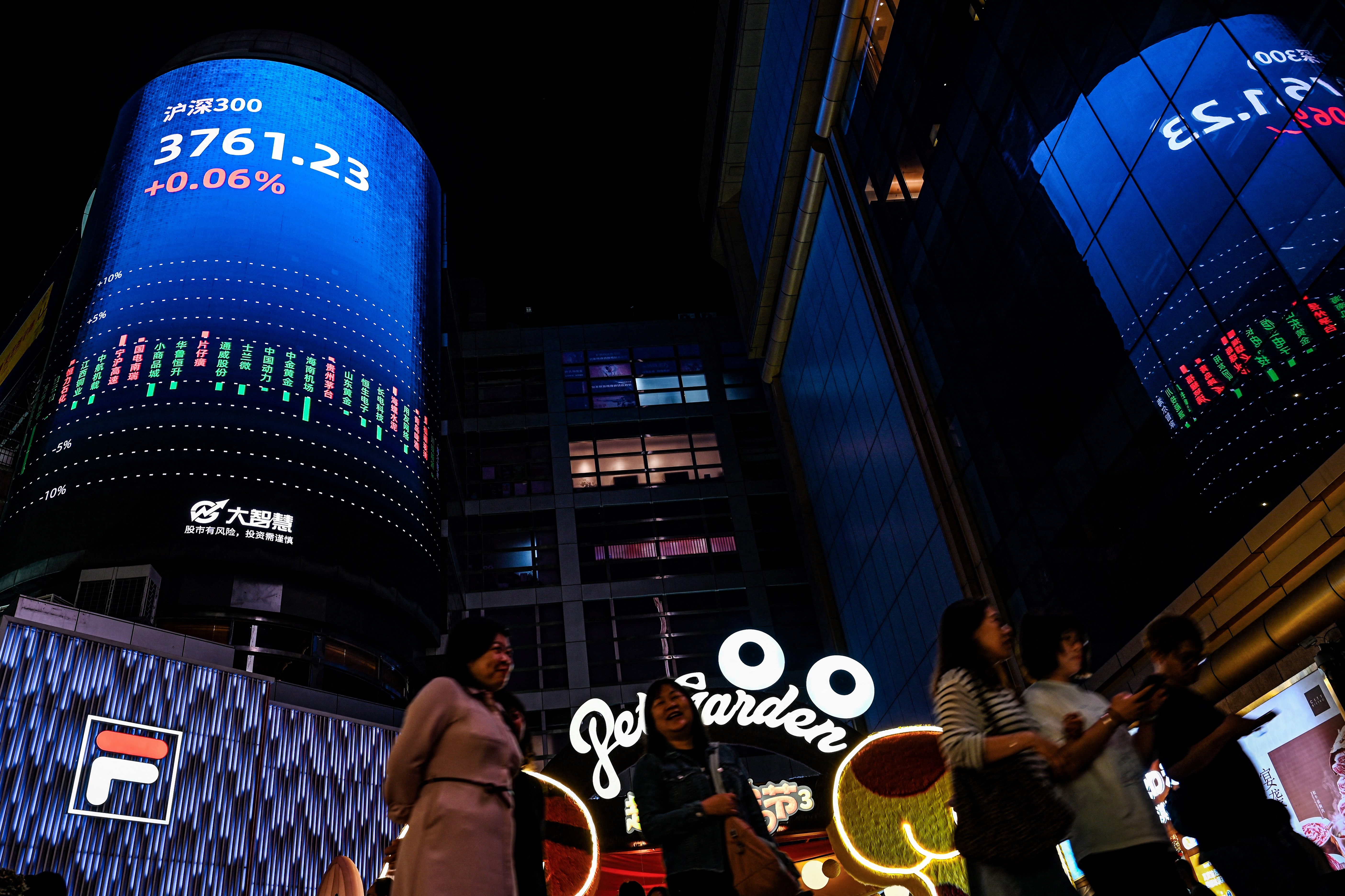 People walk past a screen showing the CSI 300 Index at a shopping mall in Guangzhou, in southern China
