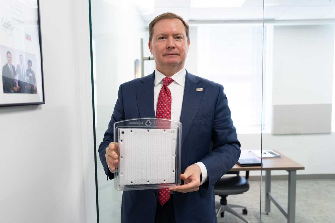 Standing in an office, Bill Steiger holds a "spatial emanator," which consists of a white, square sheet that's encased in clear plastic.