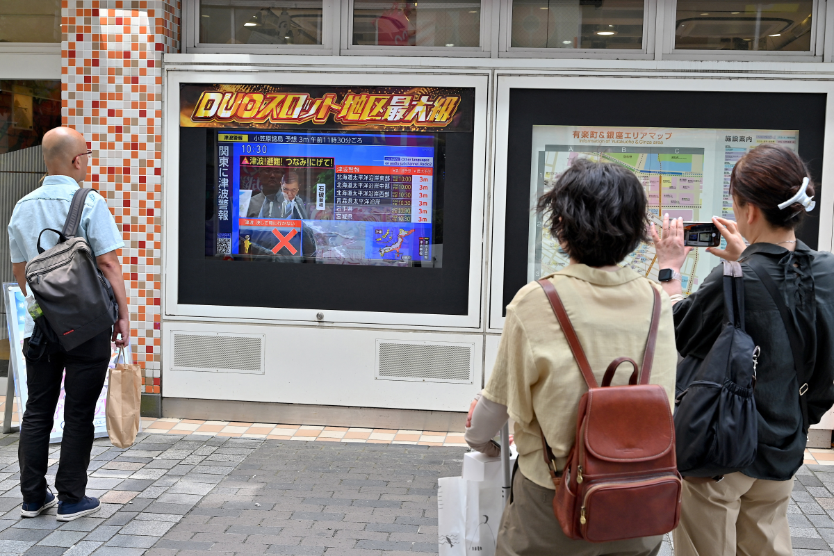 People watch a television broadcast of a tsunami warning for much of coastal Japan outside a gaming shop in central Tokyo on Wednesday.