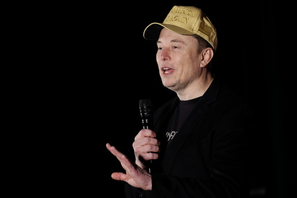 Elon Musk, dressed in black and wearing a baseball cap, wields the microphone at a town hall-style meeting in Folsom, Pa.