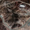 This satellite image shows an area of brown mountains in Iran, with the Fordo Fuel enrichment plant in the country integrated into one of the mountain sides. A road turns roughly the perimeter of the image.