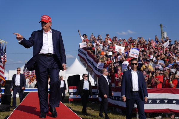 Republican presidential candidate Donald Trump arrives for the campaign rally in Butler on July 13. He's walking down a long, narrow red carpet while wearing a suit. In the background are people attending the rally.