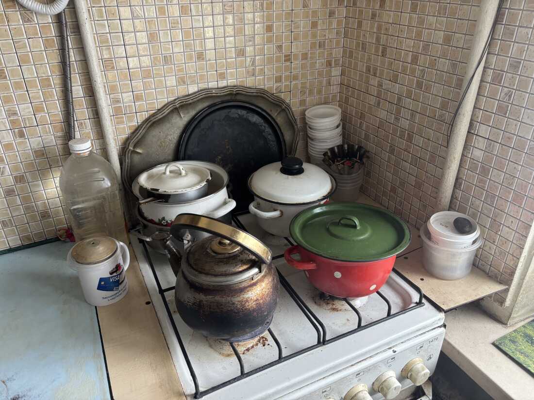 Multiple pots and a kettle sit on the four burners of a stove. The walls behind the stove and to the right of it are covered in sandy-brown tiles.