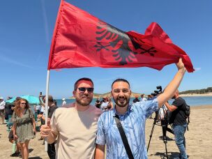 34-year-old Albanian software engineer Albi Batozi, right, holds an Albanian flag with a friend at a protest along the beach in Zvérnec, a place where Batozi says he grew up swimming.