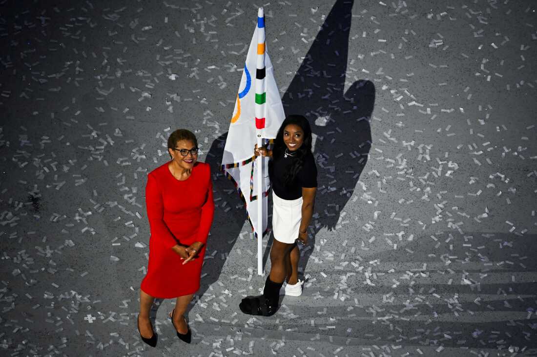 An overview shows Los Angeles Mayor Karen Bass and U.S. gymnasts Simone Biles holding the Olympic flag on Sunday.