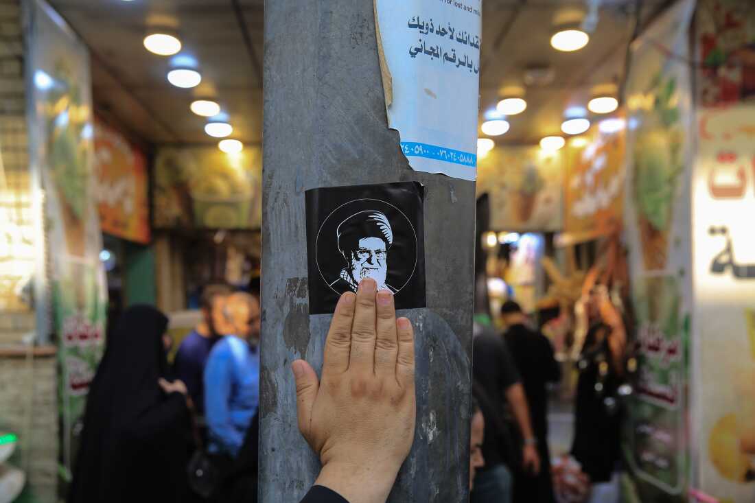 A pilgrim touches a sticker bearing a portrait of Iranian Supreme Leader Ali Khamenei affixed to a utility pole