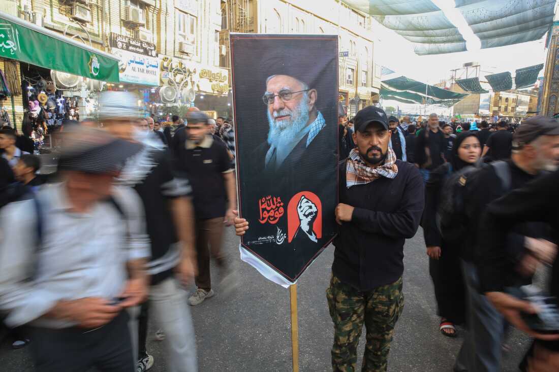 A man carries a large banner featuring a portrait of Iran’s Supreme Leader Ali Khamenei amid crowds of pilgrims on a street in Karbala during Arbaeen.