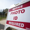 A voter walks past a sign that says "Notice: Photo ID required." 