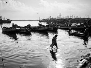A fisherman wades to the shore from his anchored boat, as the sun rises higher in the sky and the activity on the docks winds down for the day.