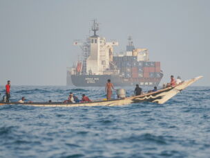People sail their boat past container ships anchoring near the Strait of Bab al-Mandeb off Yemen's coast in the Gulf of Aden on August 6, 2026.