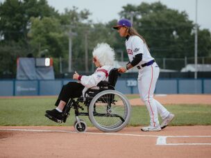 Kelsie Whitmore (right), a pitcher for the San Francisco Firebells and the league's No. 1 draft pick, guides veteran baseball player Maybelle Blair, 99, off the field after the first pitch ceremony on the WPBL's opening day.