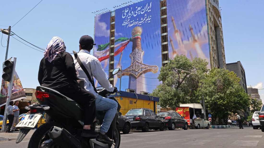 Motorists ride past a giant banner depicting Iranian missiles and a sword belonging to Imam Ali, the first Imam of the Shiites, at the Vanak Square in Tehran.
