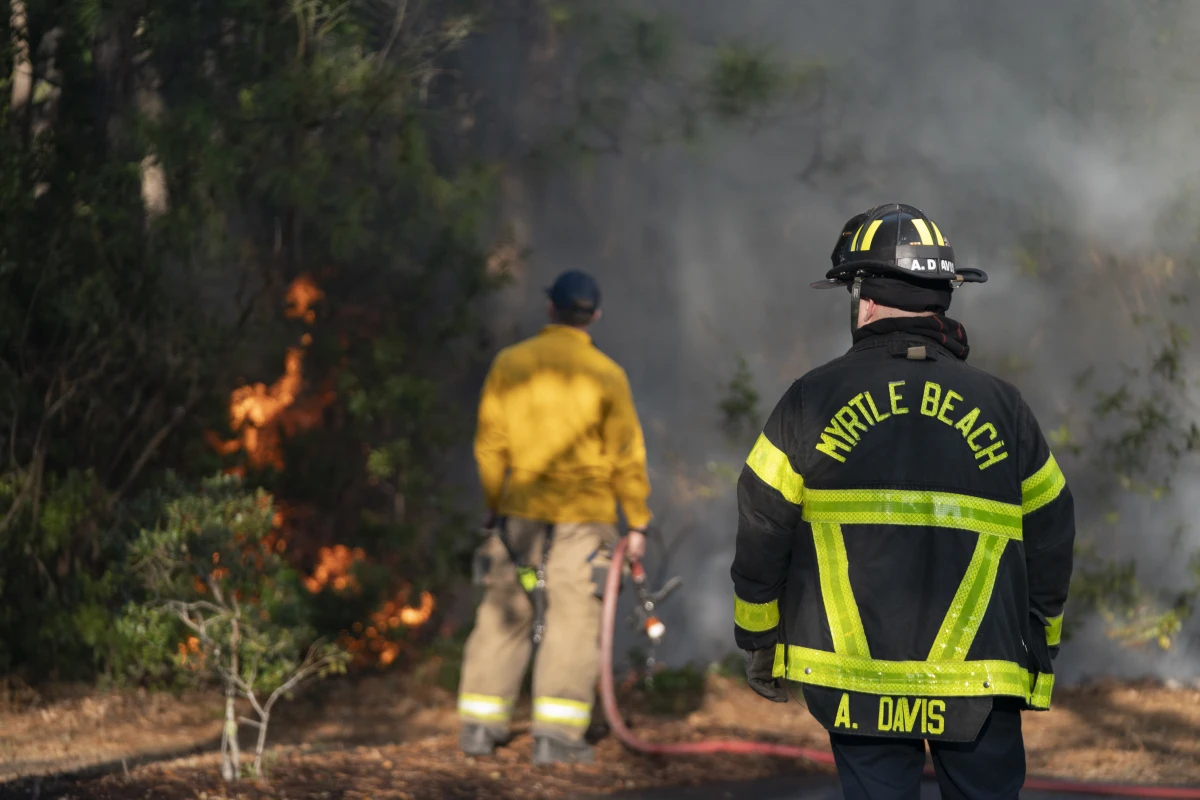 Firefighters attend to a flare-up in the Carolina Forest neighborhood on Sunday in Myrtle Beach, S.C. Multiple forest fires in the area caused evacuations along the South Carolina coast. A storm is expected to bring extreme weather and wildfire risk to various regions across the U.S. this week.