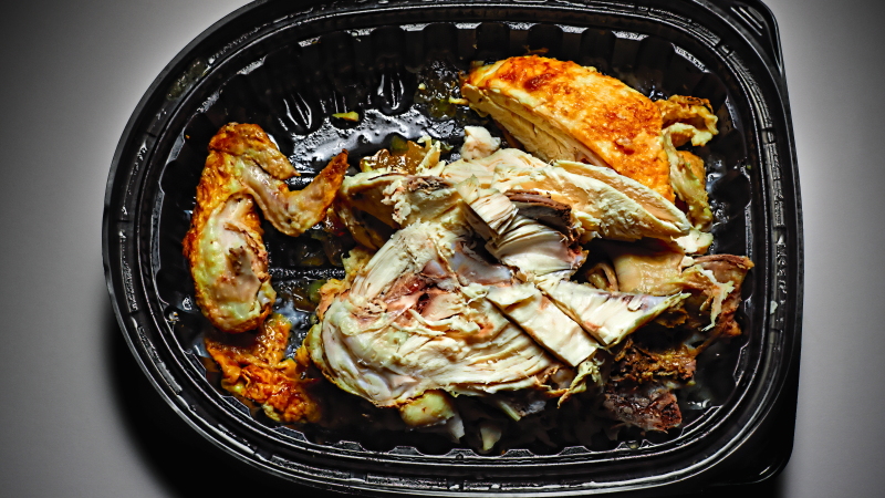 This photo shows a partially eaten chicken dish in a black plastic takeout container.