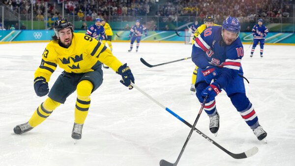 Sweden's Mika Zibanejad (93), wearing a yellow and black uniform, and U.S.'s JT Miller (10), in a red, white and blue uniform, chase the puck during the third period of a men's ice hockey quarterfinal game at the 2026 Winter Olympics.