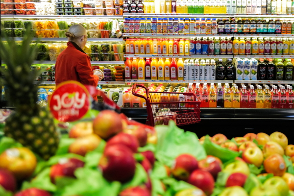 This photo shows a woman in a red coat shopping in a supermarket in New York on Jan. 27. She's facing rows of refrigerated shelves displaying bottles of juice and clear plastic tubs of chopped vegetables. Fresh fruits are on display in the foreground.