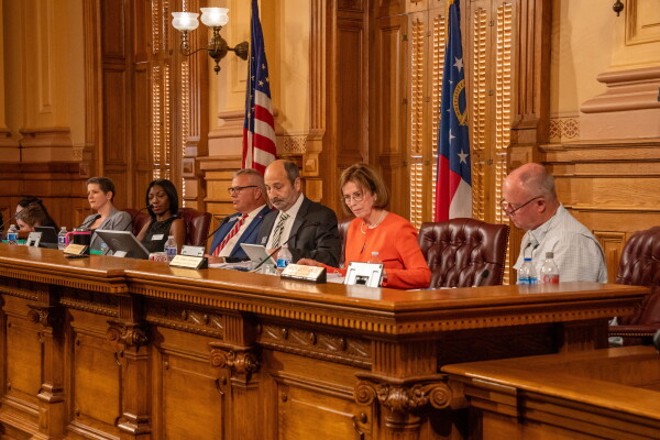 This photo shows Georgia's five-member State Election Board in August. Multiple men and women wearing business attire sit in a row in a wood-paneled room.