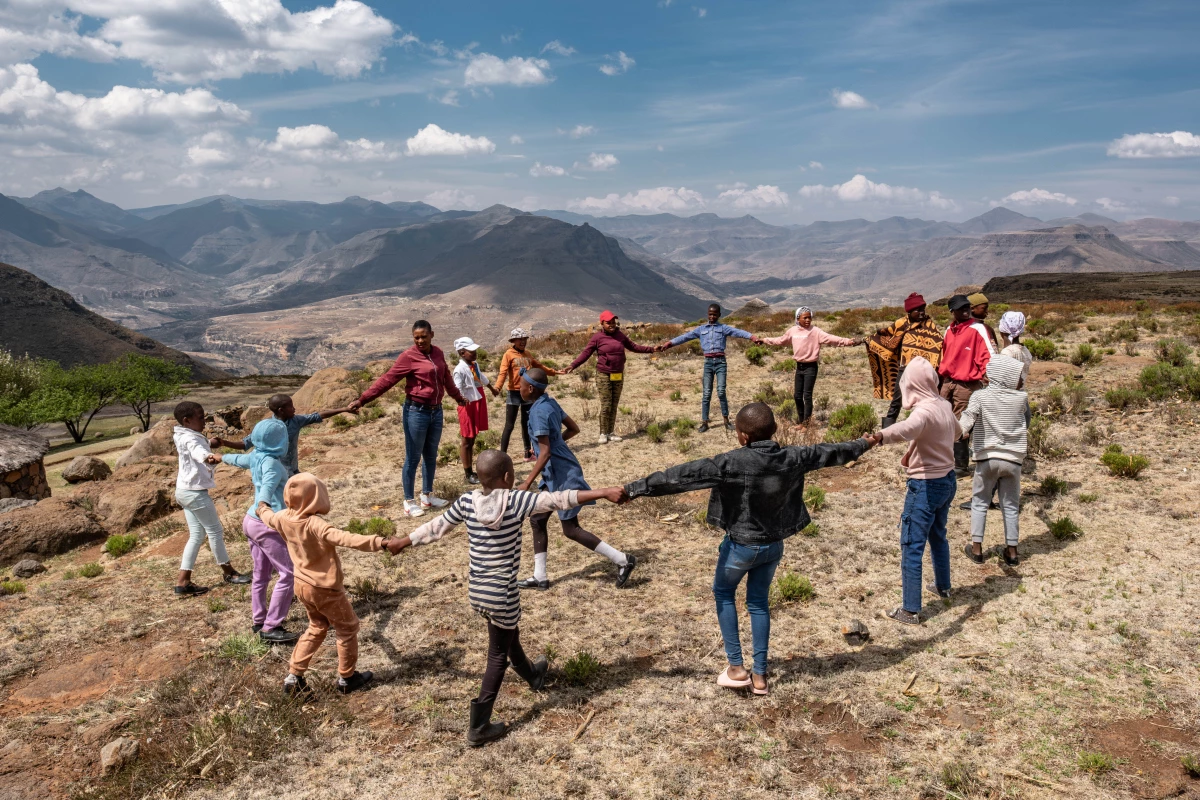 Members of a flying medical outreach team holds hands in a circle with children and teens for a session that combines fun and health education. They're in the isolated village of Ha Pheulane in the highlands of Lesotho.