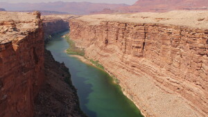 A wide bluish-green river flows through a desert canyon made of red rock