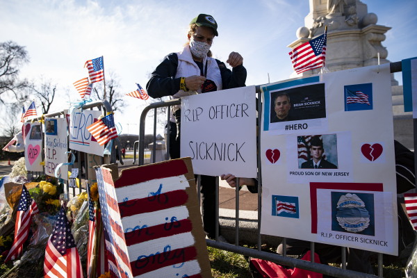 Anne Seymour, wearing a face mask, stands next to handmade signs for a memorial honoring U.S. Capitol Police Officer Brian Sicknick. Signs read "R.I.P. Officer Sicknick" and "#Hero."