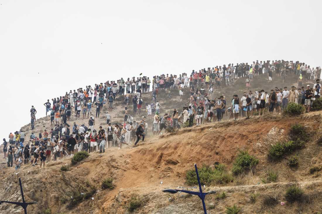 Migrants attempting to cross into Spain's North African enclave of Ceuta gather on a hilltop during clashes with Moroccan security forces near the town of Fnideq, on the Morocco-Spain border, on Friday. The European Union on July 31 scrambled to contain one of the largest migrant crises faced by the block in recent years, after tens of thousands of people poured into into Spain's North African Ceuta enclave in just days.