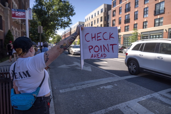People hold signs warning drivers of a checkpoint operated by the Metropolitan Police Department and federal agencies, including officers from Immigration and Customs Enforcement (ICE) and Homeland Security Investigations (HSI), on Georgia Avenue in the northern part of Washington on Aug. 30, 2025.